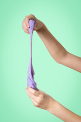 Children's hands with a lilac slime on a green background.