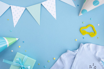 Newborn baby boy accessories and festive decoration. Birthday caps, gift box, confetti, toy car, party flags and blue clothes bodysuit. Top view, flat lay, copy space, frame