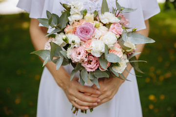  Close-up of the hands of a bride who is holding a wedding bouquet of flowers. Wedding day.