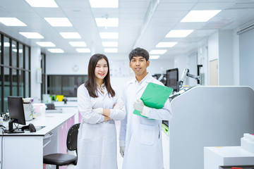 two young smiling scientist in white lab coat standing with automation blood analyzer at medical laboratory 