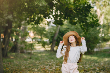 Cute little girl in a park. Child in a white blouse. Lady in a brown hat.