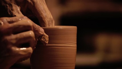 Young handsome sculptor shapes the clay product with pottery tools. Artisan potter prepares material for his pottery. Strong man hands working clay on potter's wheel. Work close-up. - Powered by Adobe
