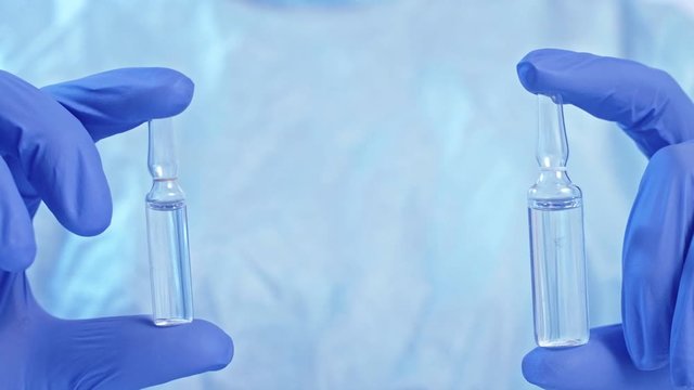 Viral vaccine. Drug manufacturing. Technician hands in gloves holding two ampoules.