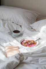Berry smoothie bowl and cup of coffee in a white bed. Work from home concept.