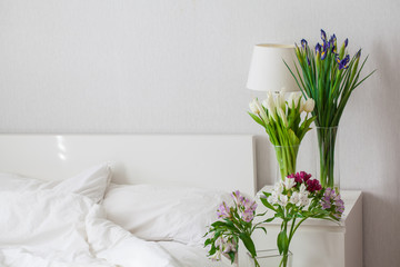Vases with flowers next to white bed. Beautiful room with spring flowers.