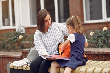 Mother and daughter. Mom puts in the backpack of baby stuff. Family sitting on a bench.
