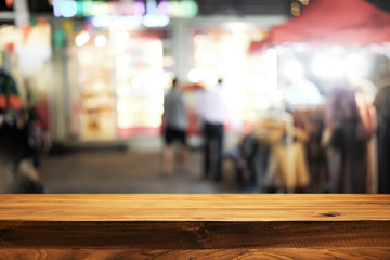 Empty wooden desk space and blurry background of street night market for product display montage.