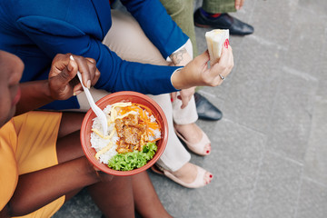 Female entrepreneurs spending lunch time outdoors and eating sandwich and rice bowl when sitting on steps