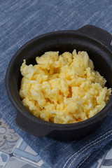 Scrambled egg in a traditional cast iron pot on a blue tea towel.  On a patterned tile surface