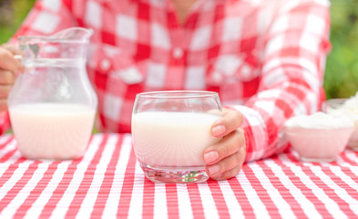 A girl in a red plaid shirt holds out a glass of milk