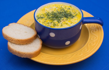 Puree soup with cheese and croutons in a blue ceramic bowl on a yellow ceramic plate on a blue background.