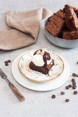 Homemade brownie with scoop of vanilla ice cream, chocolate sauce and nuts. Gray background