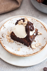 Homemade brownie with scoop of vanilla ice cream, chocolate sauce and nuts. Gray background