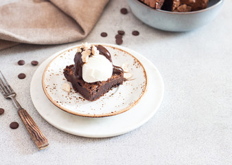 Homemade brownie with scoop of vanilla ice cream, chocolate sauce and nuts. Gray background