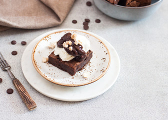 Homemade brownie with scoop of vanilla ice cream, chocolate sauce and nuts. Gray background