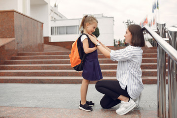 Mother and daughter. Family standing near school. Mom accompanies her child to school