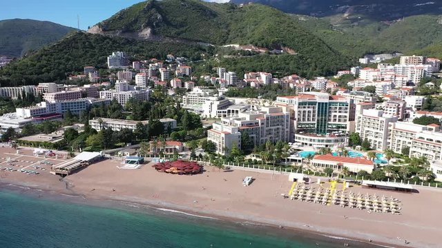 Drone footage of Becici, town near Budva, a great tourism center on Adriatic sea. Fly from sea to town, over the beach, hotels to mountain behind the town. Sunny summer day, bright and with a cloud.