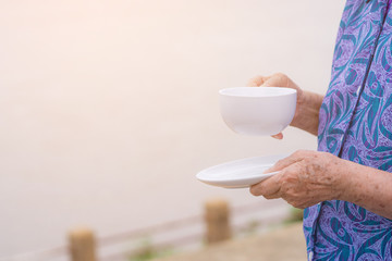 Close-up of old woman hands hold a white cup of coffee, standing at side the river. Morning coffee. Space of text