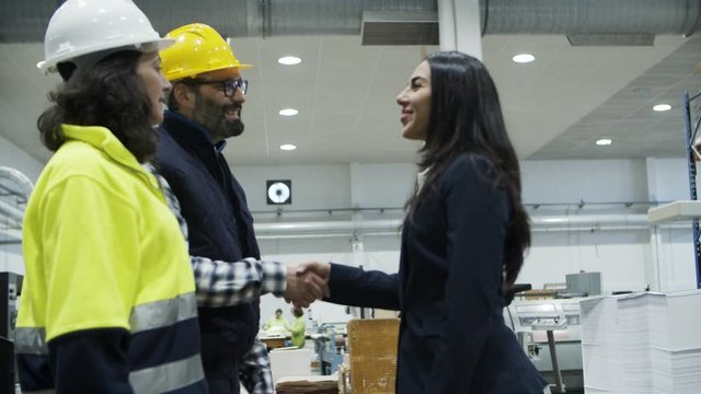Smiling project manager shaking hands with technicians. Side view of beautiful Asian woman in suit walking to factory employees and greeting. Cooperation, manufacturing, handshake concept