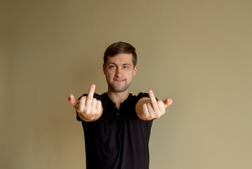 Young man in black t-shirt is showing middle finger - gesture of fuck. Expression negative, aggression, provocation.Place for text