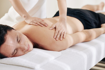 Massage therapist massaging shoulders of relaxed mature patient