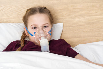girl with inhaler mask - respiratory problems for asthma. girl with a mask inhaler lies with a toy...