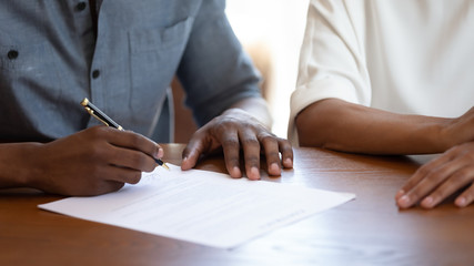 Horizontal image man holding pen put signature on agreement African couple filling form bank...