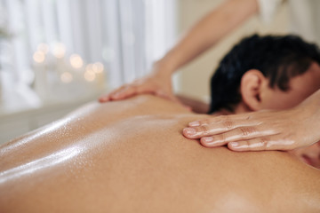 Obraz na płótnie Canvas Masseuse applying massage oil on back of male client in spa and beauty salon