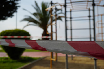Barrier red and white tape closing a passage to a street sports ground, shot close-up on a background of sports equipment. COVID-19 pandemic.