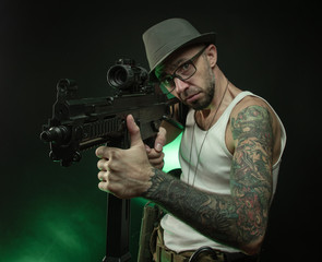 a sporty guy with a tattoo poses with an automatic rifle