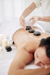 Obraz na płótnie Canvas Massage therapist putting warm massage stones along spine of spa salon client