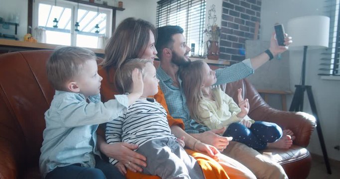 Happy young European family with three children waving to friends during smartphone video call talk at home slow motion.