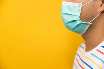 Close up young asian man wearing protection face mask against coronavirus on yellow background.