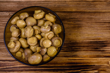 Glass bowl with canned mushrooms on wooden table. Top view