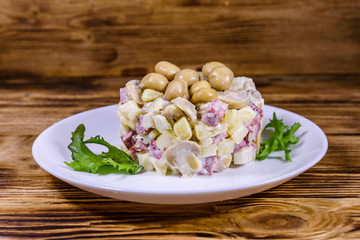 Salad with marinated mushrooms, sausage, onion, boiled potato and mayonnaise on a wooden table