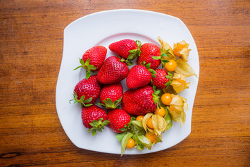 strawberries and physalis in a bowl on wood background