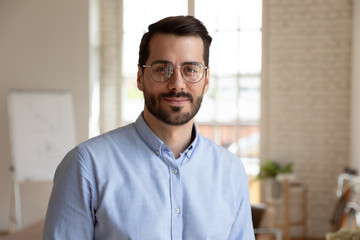 Head shot portrait of handsome bearded businessman wearing glasses looking at camera standing in office modern boardroom. Concept of successful entrepreneur, executive manager, head owner of company