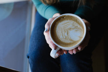 close up hand of woman holding a cup of hot big white cup of latte on jeans in the cafe