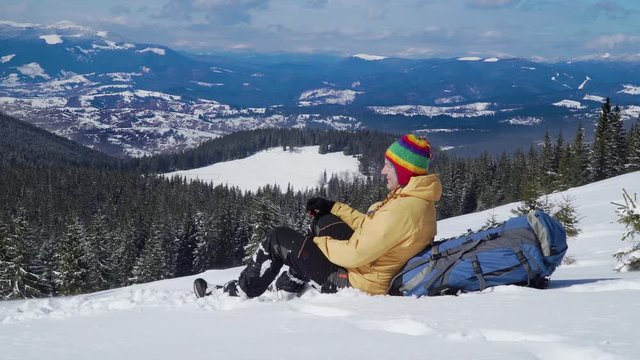 Traveller in the mountains in winter. Hiker sits in the snow and resting. Beautiful winter landscape. Carpathian mountain range. 4K