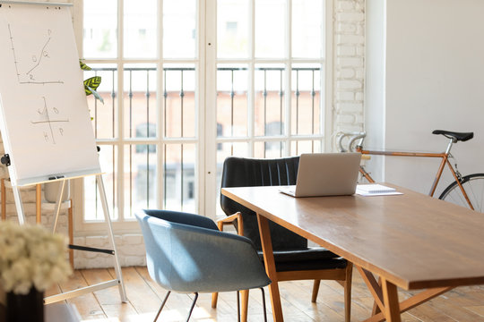 Empty Workplace No People In Modern Contemporary Light Boardroom Interior, Raised Increasing Charts On Flip Chart, Opened Laptop At Desk After Seminar, Negotiations Place For Business Meeting Concept