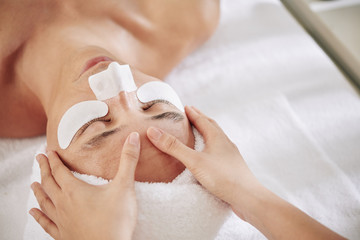 Beautician massaging forehead of mature man with horizontal wrinkles