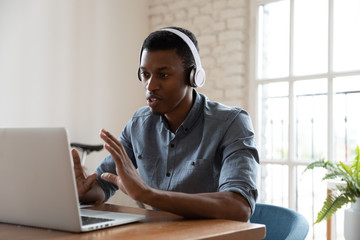 Serious confident African manager wear headphones looking at laptop screen talking provide support to client distantly, convincing customer buy company services. Student and e-learning process concept - obrazy, fototapety, plakaty