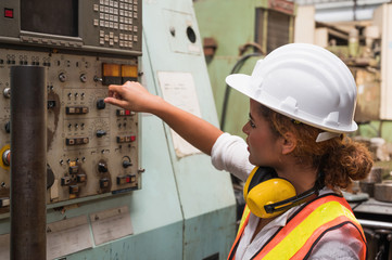 Female industrial worker working and checking machine in a large industrial factory with many equipment.