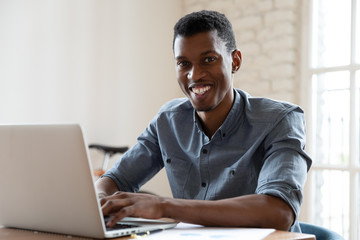 African ethnicity office worker looking at camera smiling while working at computer indoors....