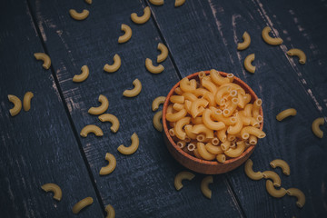Brown wooden bowl or pot with pasta or raw macaroni on black wooden background, copy space. Carbohydrates diet, healthy eating habits and vegetarian food concept.