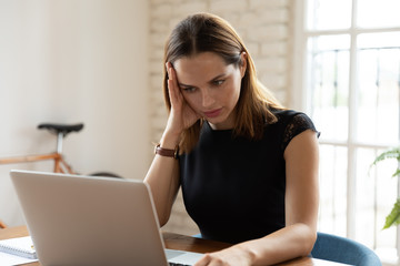 Overloaded woman sit at workplace desk touch head feels unwell suffers from headache migraine, businesswoman read unpleasant news, dismissal message, notebook broken malware, problems at work concept