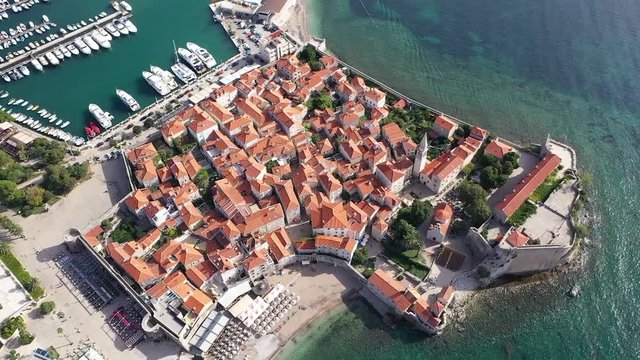 Drone footage over Budva Old Town, over yacht marine towards whole city of Budva. Sunny and bright day in summer. Old houses in Mediterranean style in Old Town and modern hotels in the City of Budva.