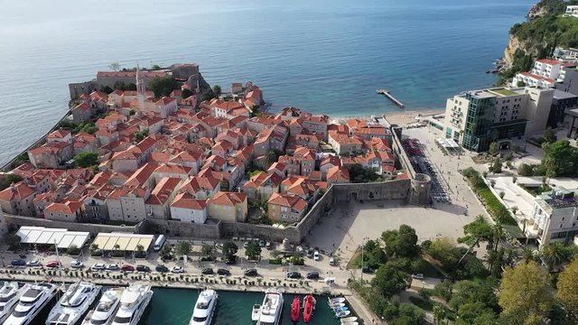 Drone footage over Budva Old Town, going to the sea.  Sunny and bright day in summer. You can see old houses in Mediterranean style. There are a beach and sea.