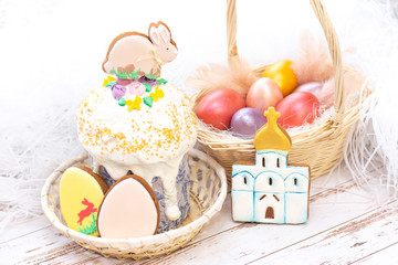Easter holiday. Colored eggs in a basket. Easter gingerbread bunny on the sandwich. Easter gingerbread cookies in the form of eggs and a temple. on a light wooden background.