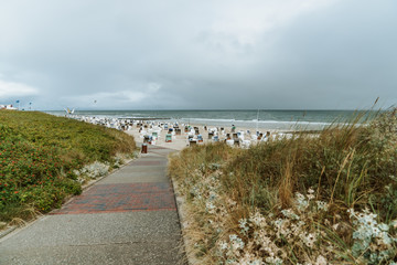 Fototapeta na wymiar A footpath through the dunes to the beach, wide beach with beach chairs, Wangerooge, Germany 